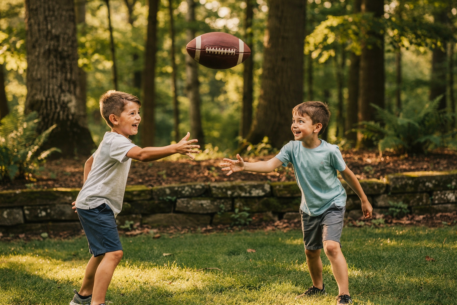 Two kids playing catch on a green lawn near the wooded edge of their backyard